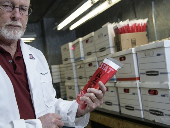 Standing inside a freezer, David Harris, PhD, shows a COVID-19 specimen collection kit inside a biohazard bag. Dr. Harris is executive director of University of Arizona Health Sciences Biorepository, and spearheaded the effort to create local testing kits so more health care providers in Arizona could administer the test to find out if patients had the virus that causes COVID-19. The effort began in March, and produced thousands of test collection kits per week.