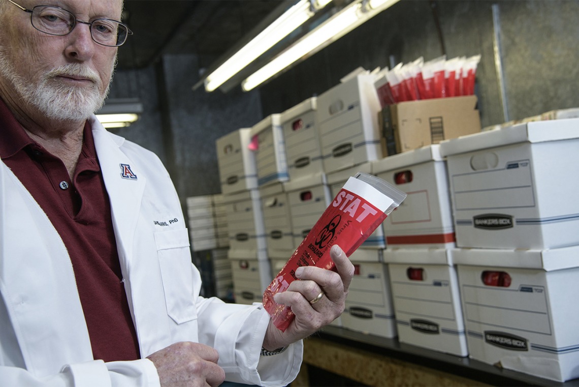 Standing inside a freezer, David Harris, PhD, shows a COVID-19 specimen collection kit inside a biohazard bag. Dr. Harris is executive director of University of Arizona Health Sciences Biorepository, and spearheaded the effort to create local testing kits so more health care providers in Arizona could administer the test to find out if patients had the virus that causes COVID-19. The effort began in March, and produced thousands of test collection kits per week.