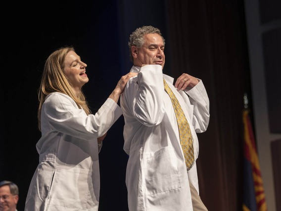 Professor Lindsay Bouchard helps Michael Nango with his white coat at the UArizona College of Nursing white coat ceremony.