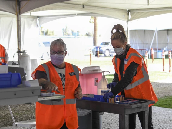 Volunteer Becky Dillie, left, prepares to log information in her computer as volunteer Kerry Johnson sets up to provide vaccinations to drivers with appointments. 