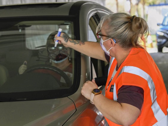 After receiving a vaccine, each driver must wait 15 minutes in their car to ensure no immediate side effects. At the University of Arizona vaccine distribution site, a volunteer writes the vaccination time on a driver’s window.