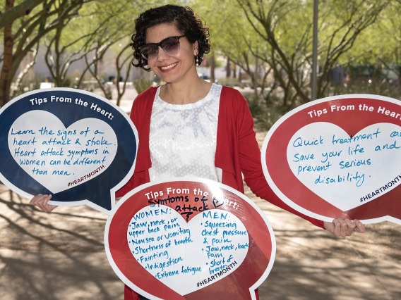 Female professor with dark curly hair wearing sunglasses holds three heart-shaped posters. 