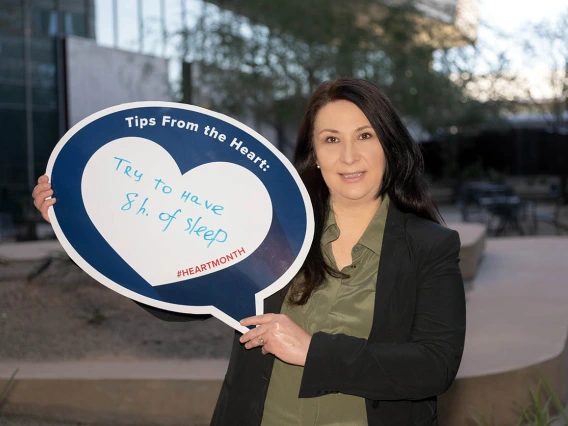 Woman with shoulder-length dark hair holds up sign saying "Try to have 8 hours of sleep"