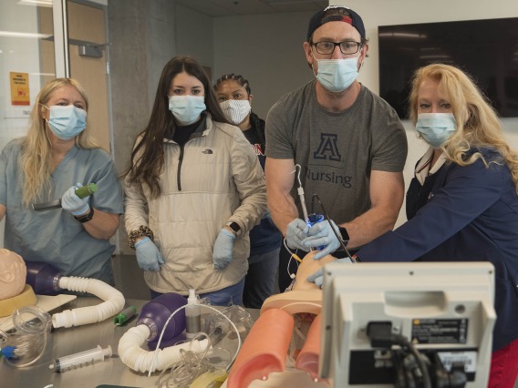 (From left) First year CRNA students Jennifer Heiden, Cameron Wylie and Sabrena Wells (back) observe as Phillip Witte practices performing a GlideScope intubation alongside Kristie Hoch, DNP, CRNA, MS, RRT, at the Arizona Simulation Technology and Education Center. Dr. Hoch is the program administrator for the nurse anesthesia program at the College of Nursing. 
