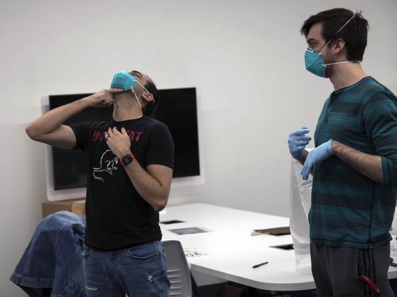 Second-year College of Medicine – Tucson student Alexandre Cavalcante adjusts his N95 mask as student-volunteer Billy Evans watches.