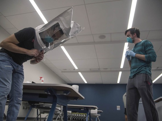 Under the watchful eye of student-volunteer Billy Evans, second-year College of Medicine – Tucson student Alexandre Cavalcante bends over while wearing a hood and his N95 mask. This is one of seven exercises the students must do during the mask-fit test. 