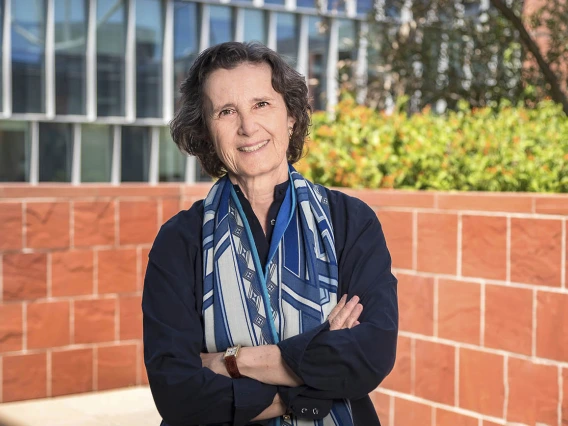 Smiling woman in dark blouse and scarf standing outside with arms crossed. 