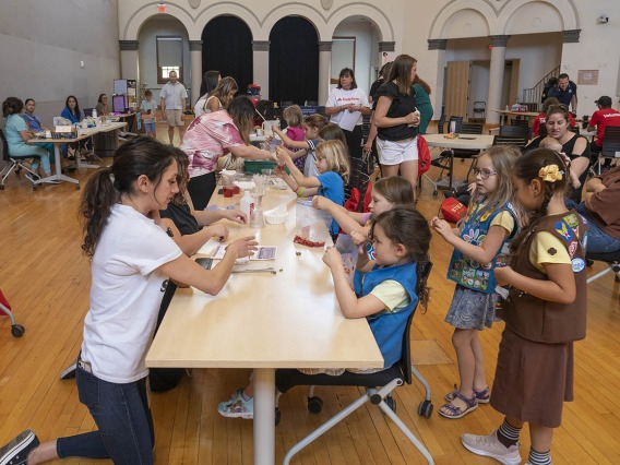A large room filled with activity tables, volunteers and girl scouts. 
