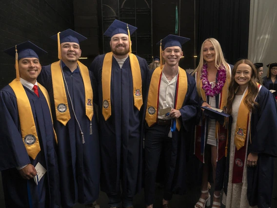 Six people (four male and two female) smile together backstage in Centennial Hall before convocation.