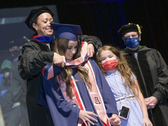 Gliney Clarissa Rios, MPH, accompanied by her daughter Mia, is hooded during the 2022 Mel and Enid Zuckerman College of Public Health spring convocation. 
