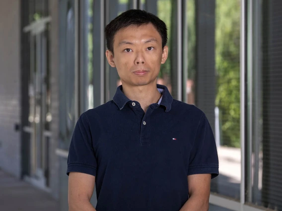 Asian man with dark brown hair and wearing a black t-shirt stands outside.