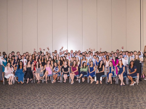 A group of 120 new medical students pose for a photo in large group sitting and standing. 