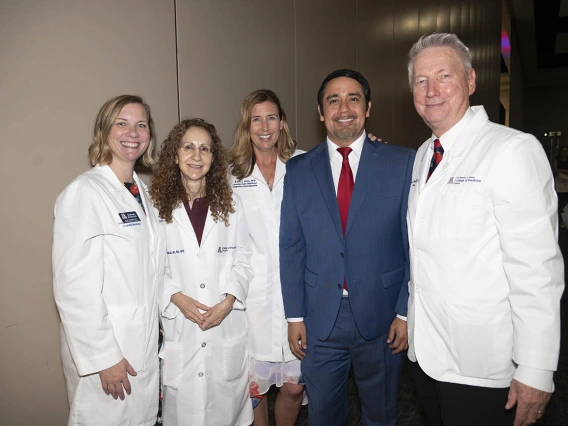 Five medical school faculty members, women and men, mostly wearing white coats stand together smiling. 