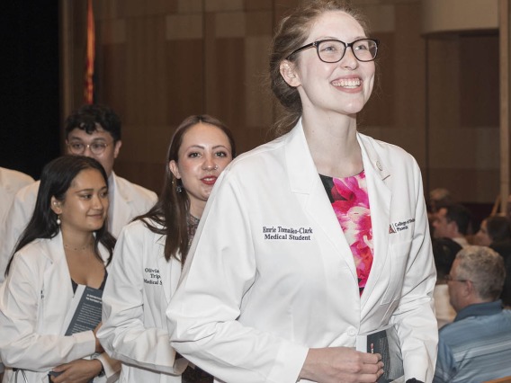 A very happy Emrie Tomaiko-Clark walks out of Symphony Hall in a procession after the UArizona College of Medicine – Phoenix Class of 2026 white coat ceremony in downtown Phoenix.