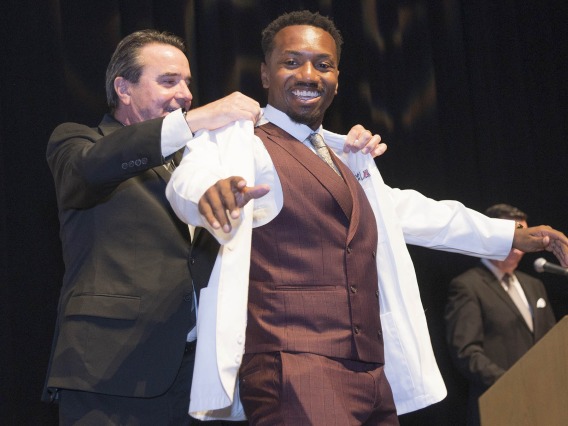 Paul R. Standley, PhD, associate dean of curricular affairs and program evaluation at the UArizona College of Medicine – Phoenix, presents Javon Maceo Freeman with his white coat.
