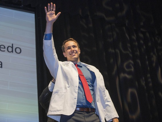 Santiago Robledo Logan-Baca waves to his family from the stage after receiving his white coat during the UArizona College of Medicine – Phoenix Class of 2026 white coat ceremony.