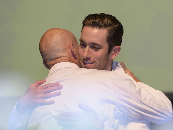 Two male medical school professors wearing white coats hug. 