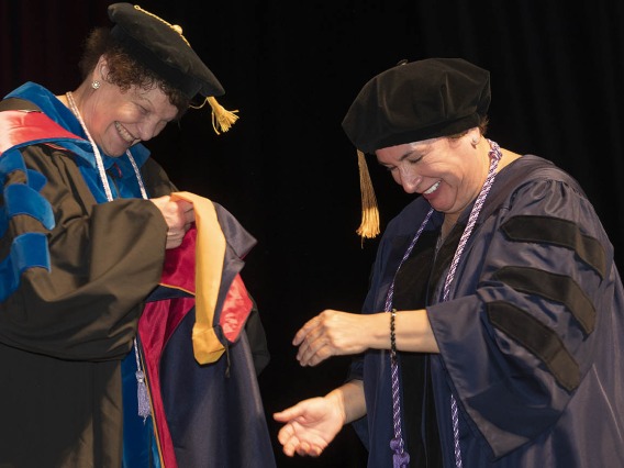 Nicolette Ann Estrada, PhD, MAOM, FNP, (left) an assistant clinical professor in the College of Nursing, prepares to hood Ana Marie Rivera, who earned a Doctor of Nursing Practice degree.