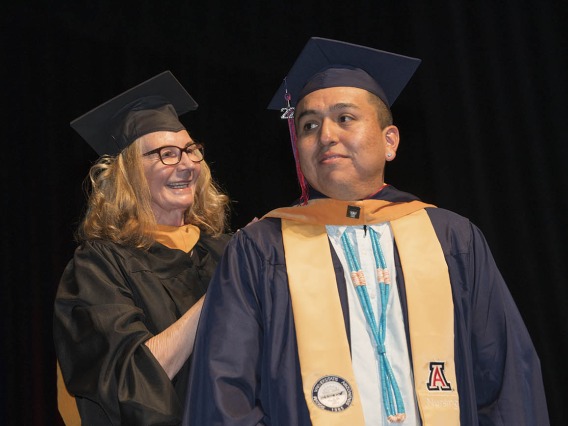 College of Nursing principal lecturer Karen Butterbaugh, MSN, hoods Ryan Whitehorse, who earned a master’s degree in nursing entry to the profession.