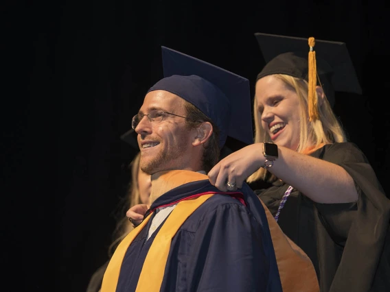 Master of Science in Nursing Entry to the Profession student Marshall Willy-Gravley is hooded by senior lecturer Heidi Kosanke, MSN/Ed, CCRN, during the College of Nursing’s 2022 summer convocation.