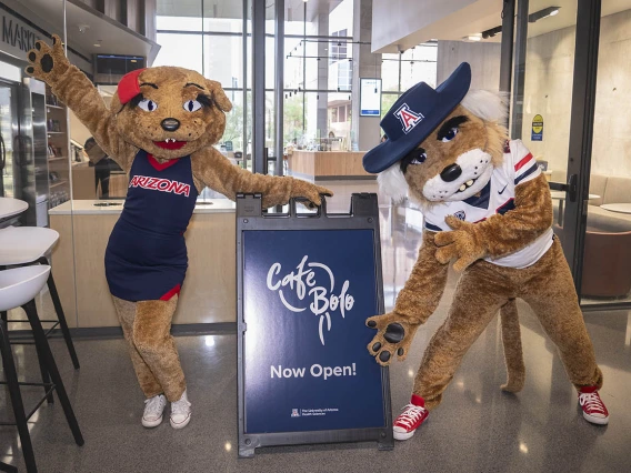 Wilma and Wilbur Wildcat maskcots standing next to a Cafe Bolo sign. 