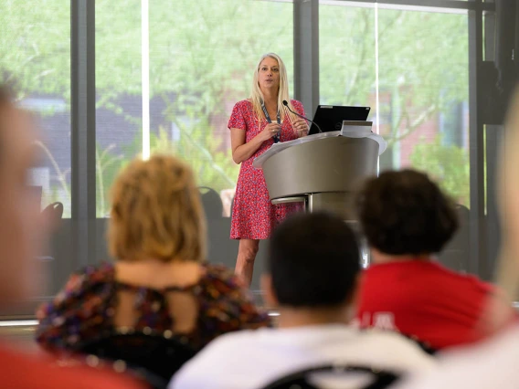 Kelly Reynolds, PhD, stands at a podium speaking to a croud. 