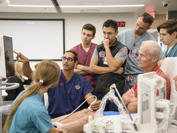 Emergency medicine residents gather around a standardized patient to learn how to administer ultrasound for different injuries.