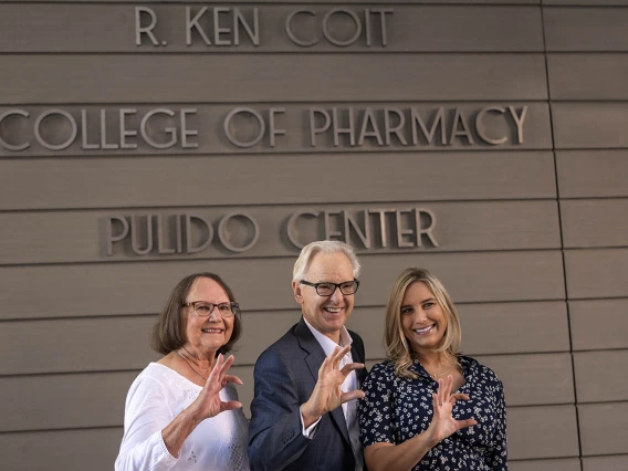 Donna Coit, R. Ken Coit and daughter Lauryn Coit Ackley give the Wildcat sign in front of the newly named R. Ken Coit College of Pharmacy. 