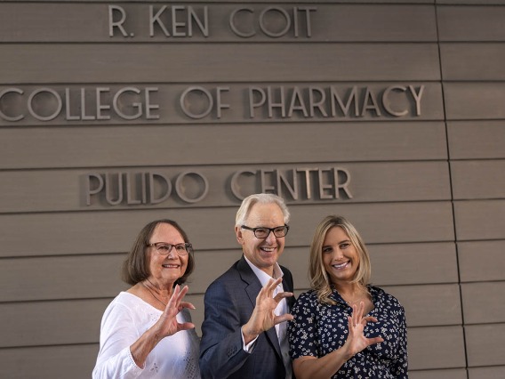 Donna Coit, R. Ken Coit and daughter Lauryn Coit Ackley give the Wildcat sign in front of the newly named R. Ken Coit College of Pharmacy. 