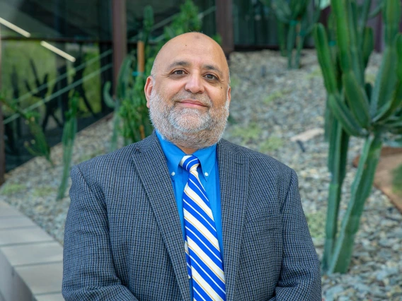 Dr. Shakaib Rehman smiling. He is wearing a blue dress shirt, grey suit jacket and blue and yellow tie.