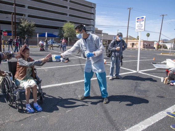 Christian Bergman and Shrey Goel offer a drink to a person in the parking lot of the Z Mansion, a soup kitchen for Tucson’s homeless population.