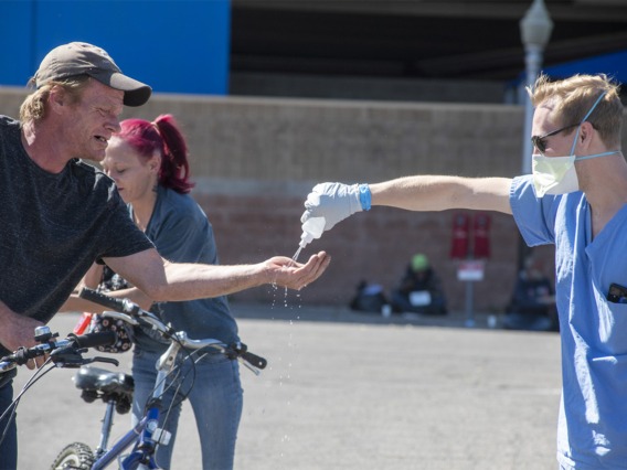 A student in the College of Medicine – Tucson helps a man sanitize his hands. Students are helping homeless people during the pandemic, because the medically-vulnerable population is expected to be hit hard by the COVID-19 virus.