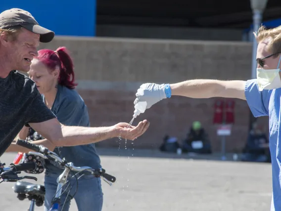 A student in the College of Medicine – Tucson helps a man sanitize his hands. Students are helping homeless people during the pandemic, because the medically-vulnerable population is expected to be hit hard by the COVID-19 virus.