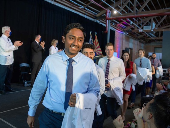 Lucky Surendra, Armin Talle, Gregory Sprout, Hannah Tolson, Tyler Vail and Ankedo Warda enter the white coat ceremony in front of seated friends and family.