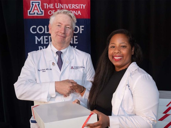 Dean Guy Reed, MD, MS, presents Jade Parker-Character with a box containing medical scrubs during the ceremony.