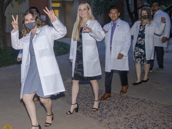 Issa Jimenez Espinoza gives two V signs as she and her classmates Megan Taylor, Brenn Belone, Lacey Hart and Curtis Mcguire leave Centennial Hall after participating in the Class of 2025 white coat ceremony.
