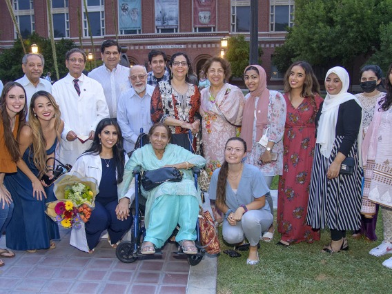 UArizona College of Medicine – Tucson’s Duri Sabina Saeed, kneeling with flowers, poses for a photo with her family and friends after the Class of 2025 white coat ceremony at Centennial Hall.