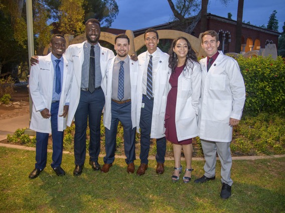 UArizona College of Medicine – Tucson classmates, from left, Toluwalase Talabi, Ayomide Odeneye, Ben Litmanovich, Sascha Delzepich, Aseel Ibrahim and Max Coffeen pose for a photo outside of Centennial Hall after receiving their white coats.