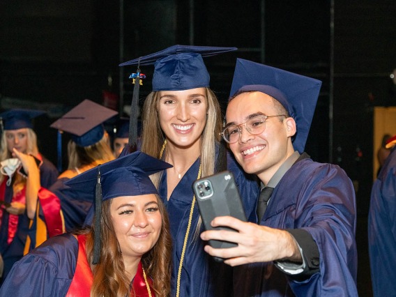From left, Ivana Matovic, Allison Gilbert and Aaron Gomez take a selfie before the start of the August commencement ceremony at Centennial Hall.