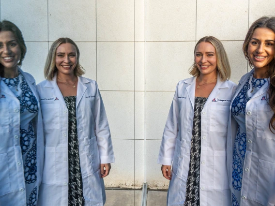 Danielle Crooke and Sarah Bricker (dark hair) are reflected in a window outside of Crowder Hall after their Doctor of Nursing Practice white coat ceremony. 