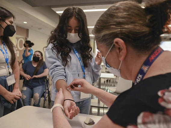 Colette Scott, director of Interprofessional Clinical and Professional Skills Center, right, uses makeup to create a bruising affect on ACES camper Isabella Espinoza. The campers then went into their clinical practice presenting with bruising. 