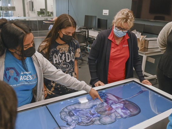 ASTEC’s Deana Ann Smith, RN, (second from right) shows students the Anatomage table in the ASTEC lab, where students practiced dissecting a digital body. 