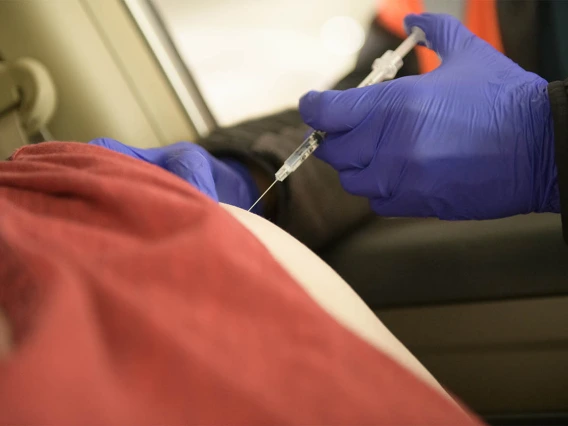 Kerry Johnson administers the COVID-19 vaccine while the recipient remains in their vehicle.