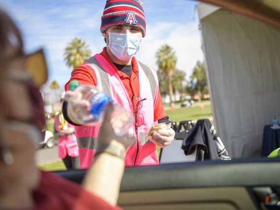 UArizona employee Brandon Goldstein hands out bottles of water and crackers for those waiting in an observation lot after being vaccinated.