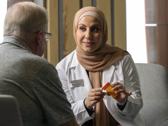 Diyana Ahmad, a second-year student at the Coit College of Pharmacy, holds a prescription bottle and discusses the medication with a male older adult patient.