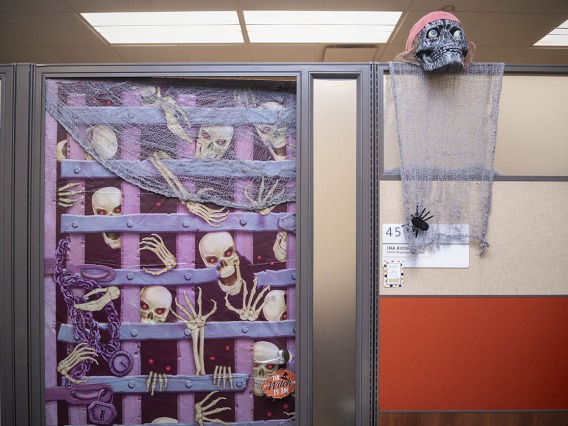 A cubicle wall with an image of an iron gate with skeletons trying to get through it. 
