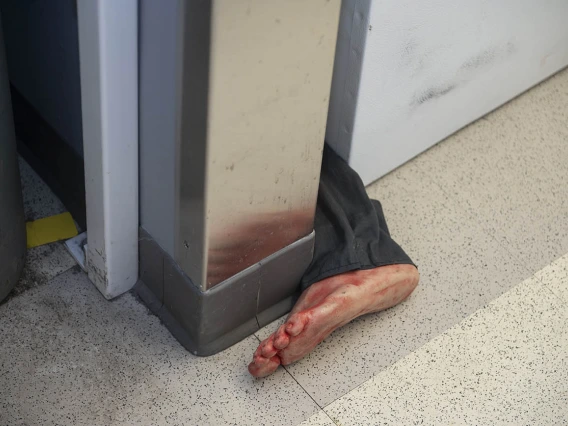 The lower part of a pantleg with a bloody foot sticks out from between a wall and piece of furniture. 