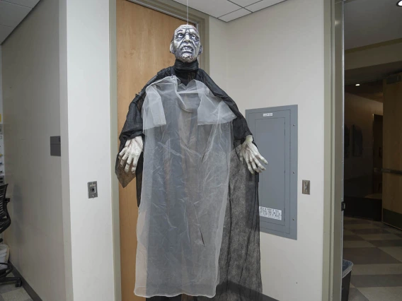 A very tall zomby in a black robe stands in a hallway of a lab.
