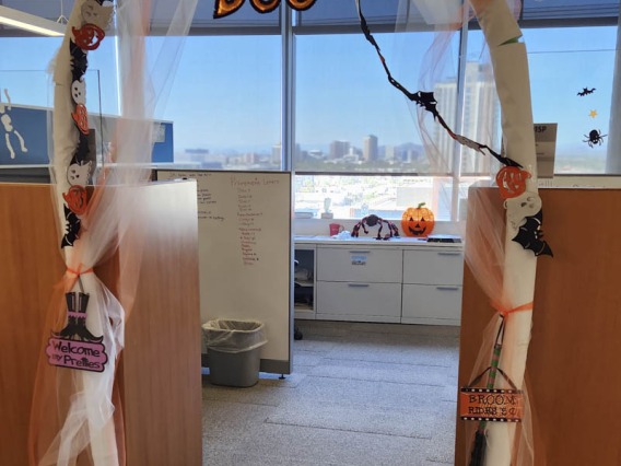 Halloween decorations create an archway between cubicles in an office. the word "Boo" hangs from the top.
