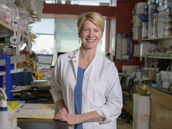 Portrait of Dr. Felicia Goodrum, a white woman with short blonde hair wearing a white lab coat and smiling while standing in her lab.